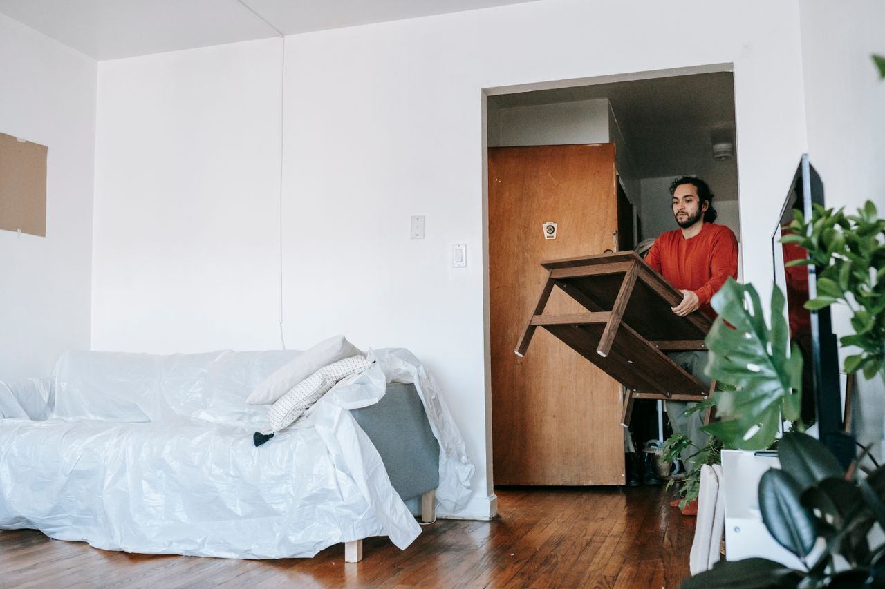 about-01 A man is carrying a wooden table while relocating inside a modern apartment.